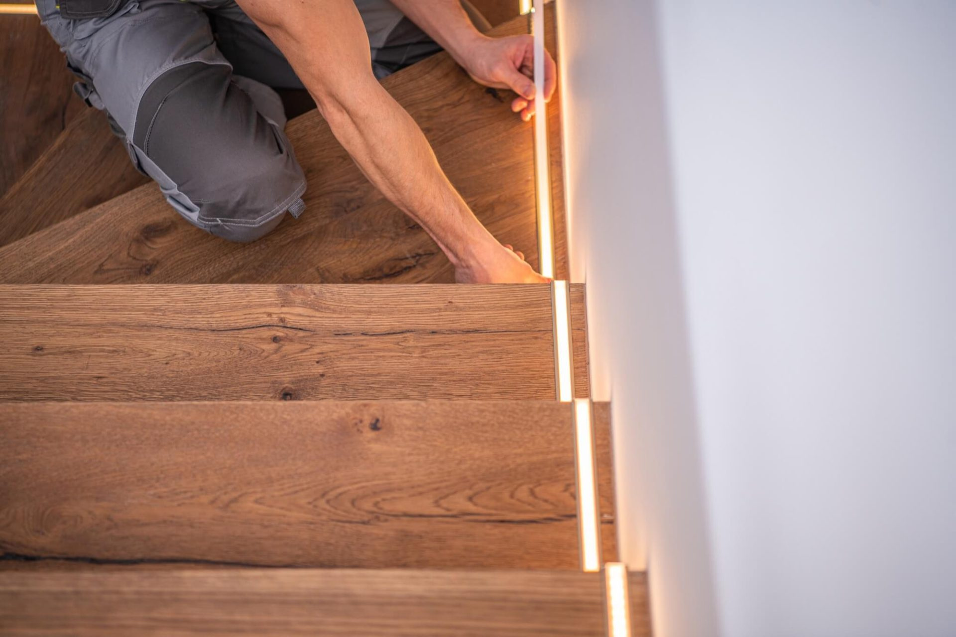 Närbild på en hantverkare som installerar en LED-list i en trätrappa som en del av en modern trapprenovering.
