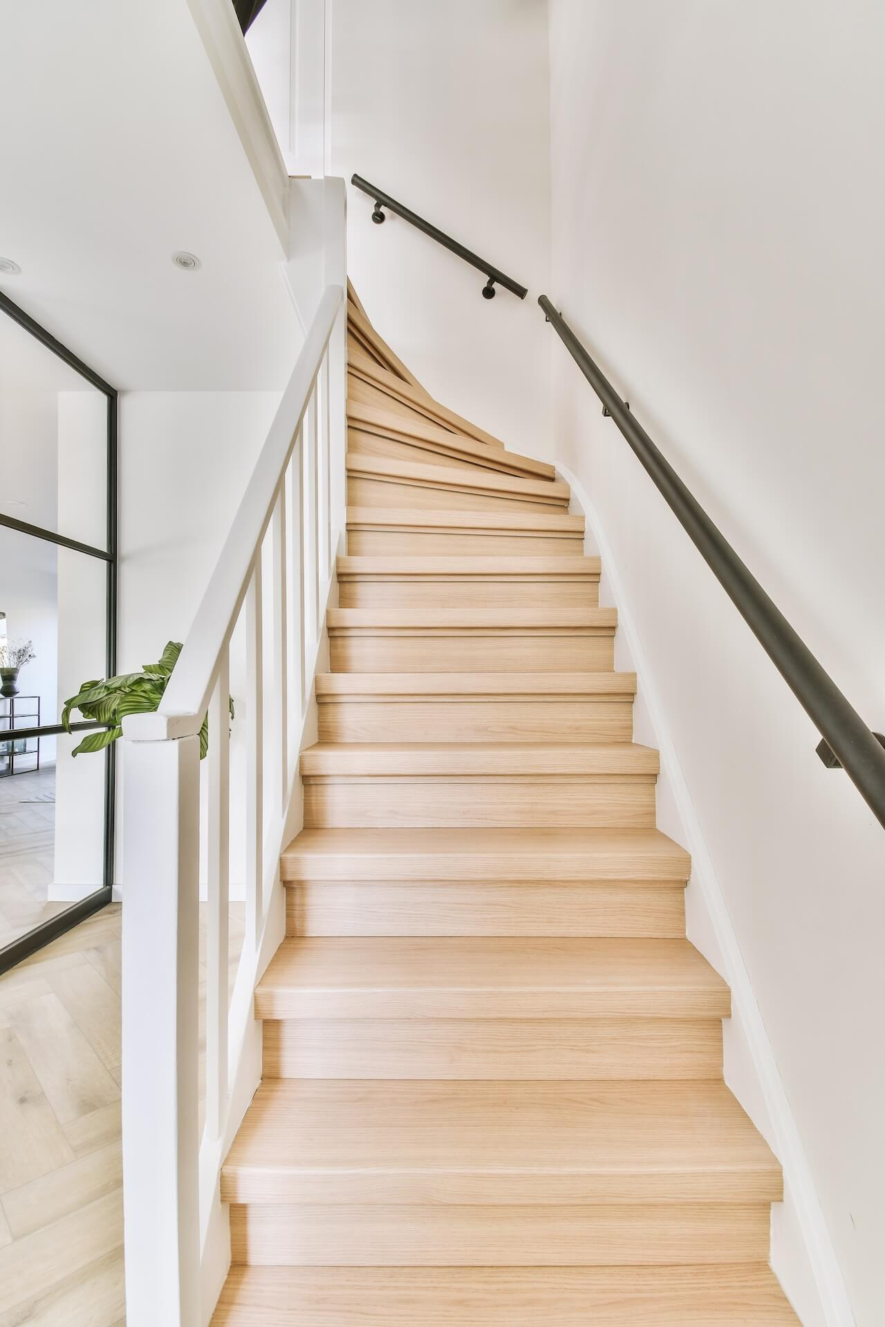 En ljus och inbjudande trätrappa med vitt räcke och svart ledstång, ett exempel på en lyckad trapprenovering.