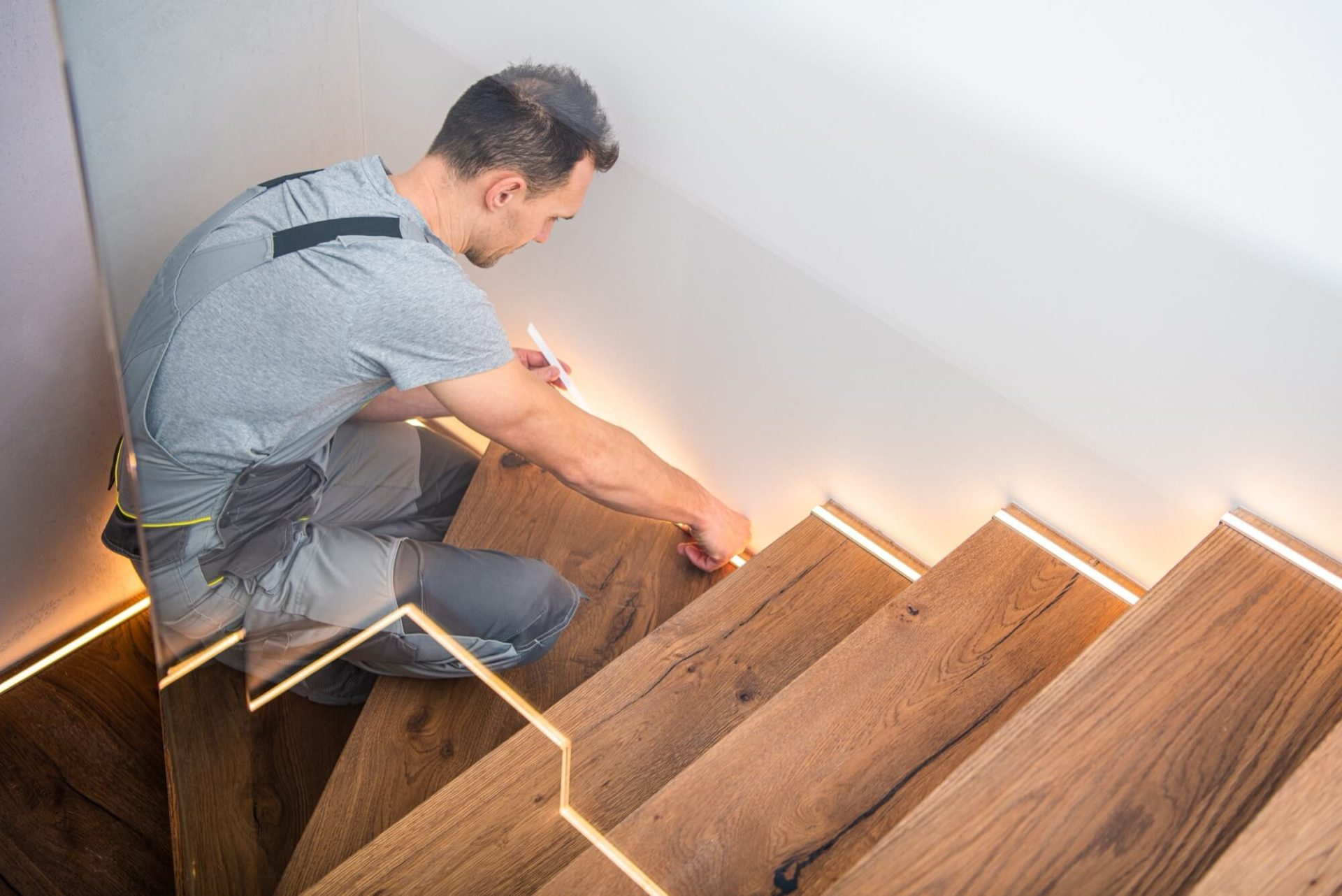 En man som utför en trapprenovering genom att noggrant installera integrerad belysning i en trätrappa.