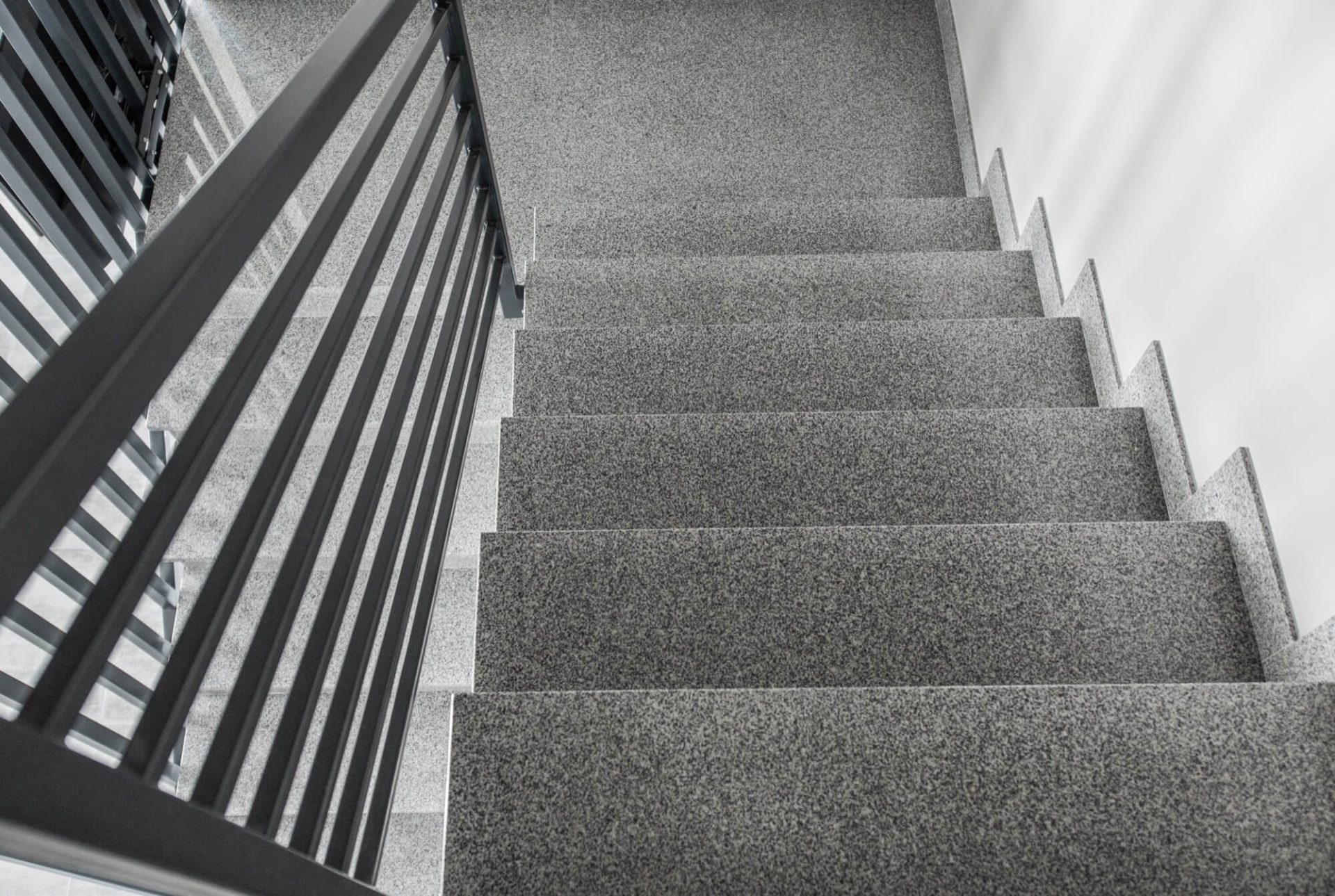 En stilren grå stentrappa med ett svart, modernt metallräcke, ett elegant alternativ för trapprenovering.