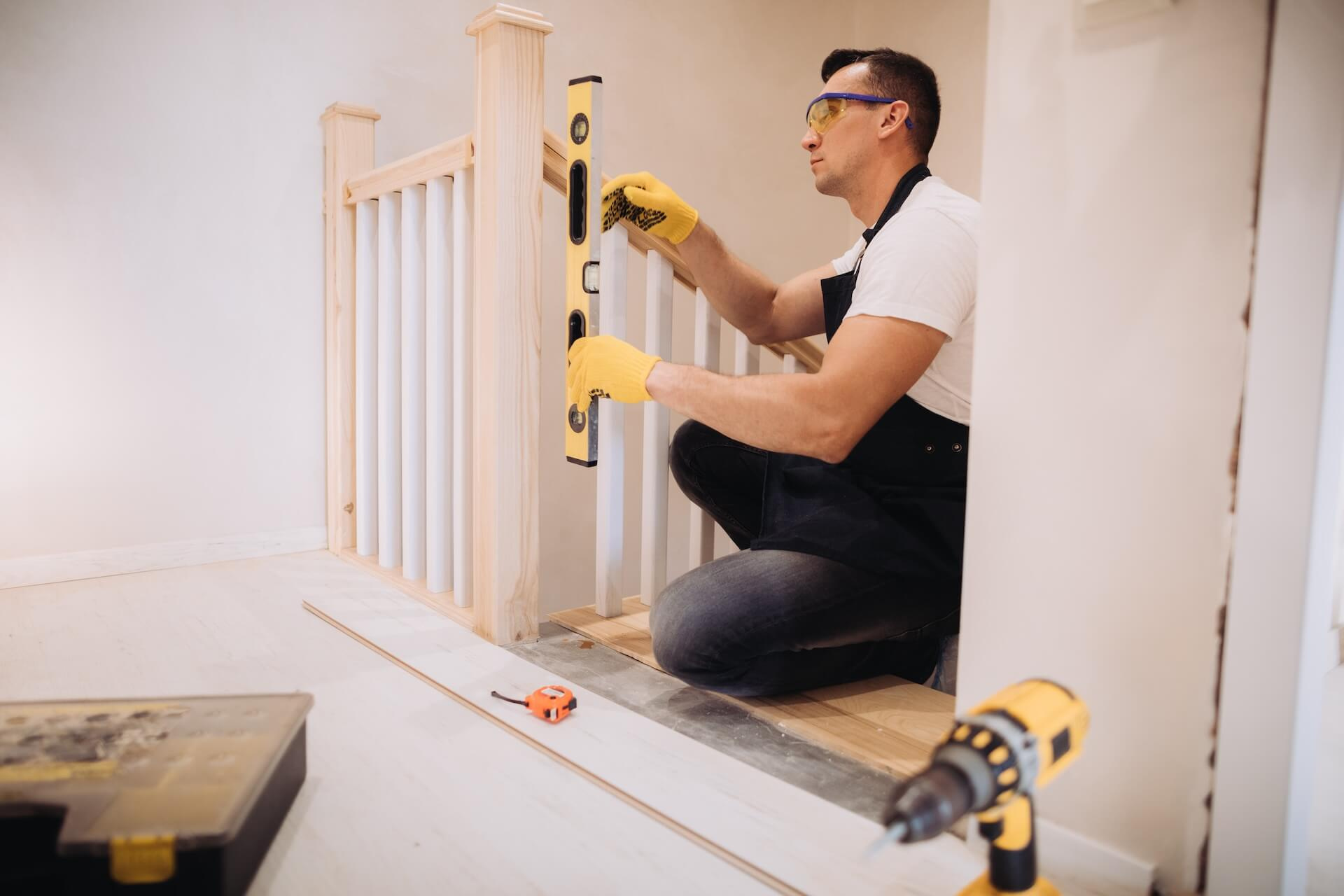 En hantverkare som säkerställer att ett nytt trappräcke är rakt med ett vattenpass under en pågående trapprenovering.