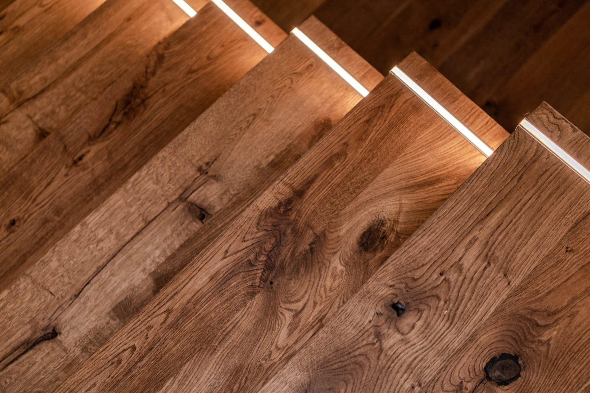 Närbild på trappsteg i mörkt trä med infälld LED-belysning, ett detaljexempel från en lyckad trapprenovering.