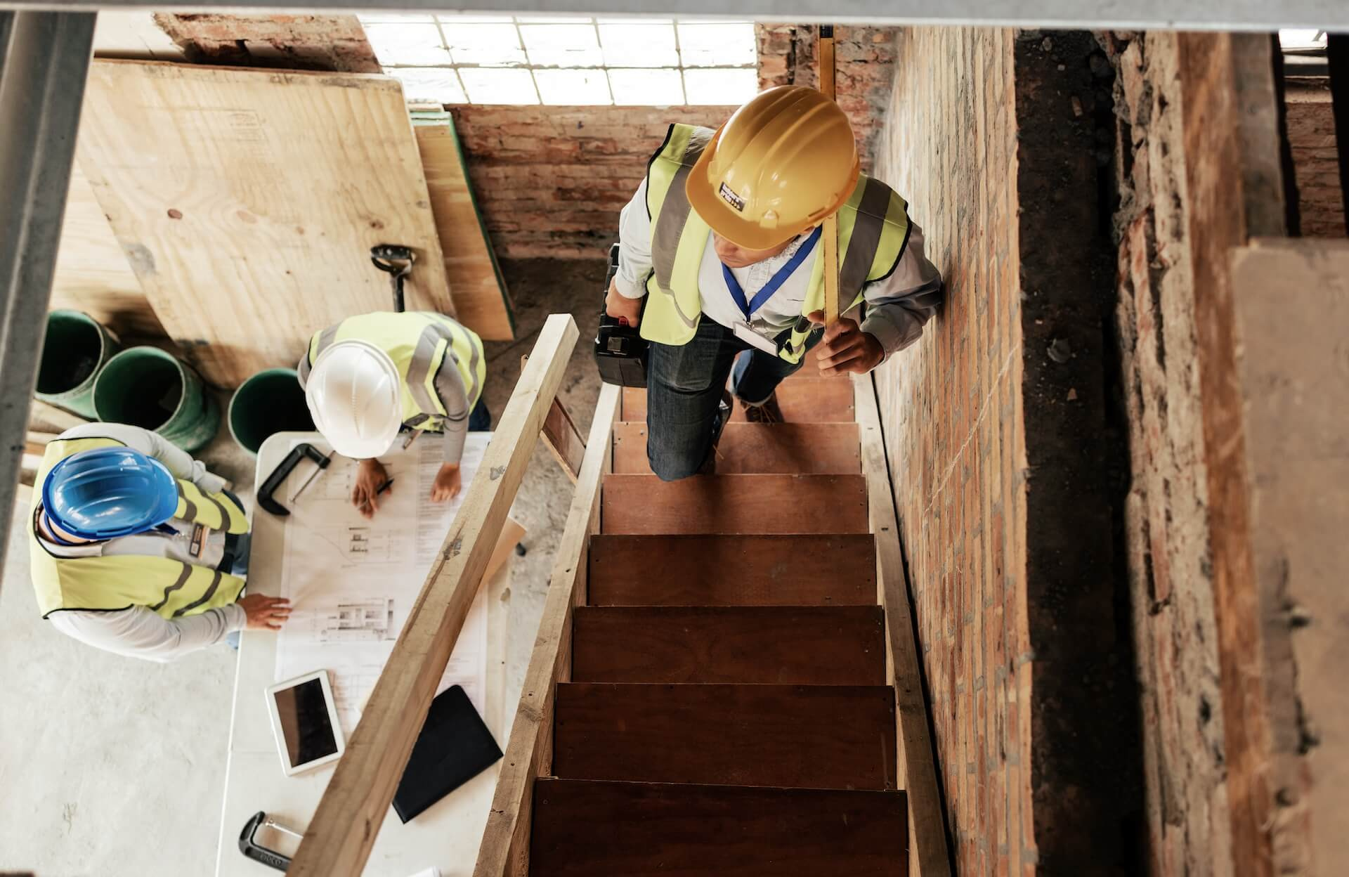 Tre byggarbetare som planerar en trapprenovering genom att titta på ritningar på en byggarbetsplats.