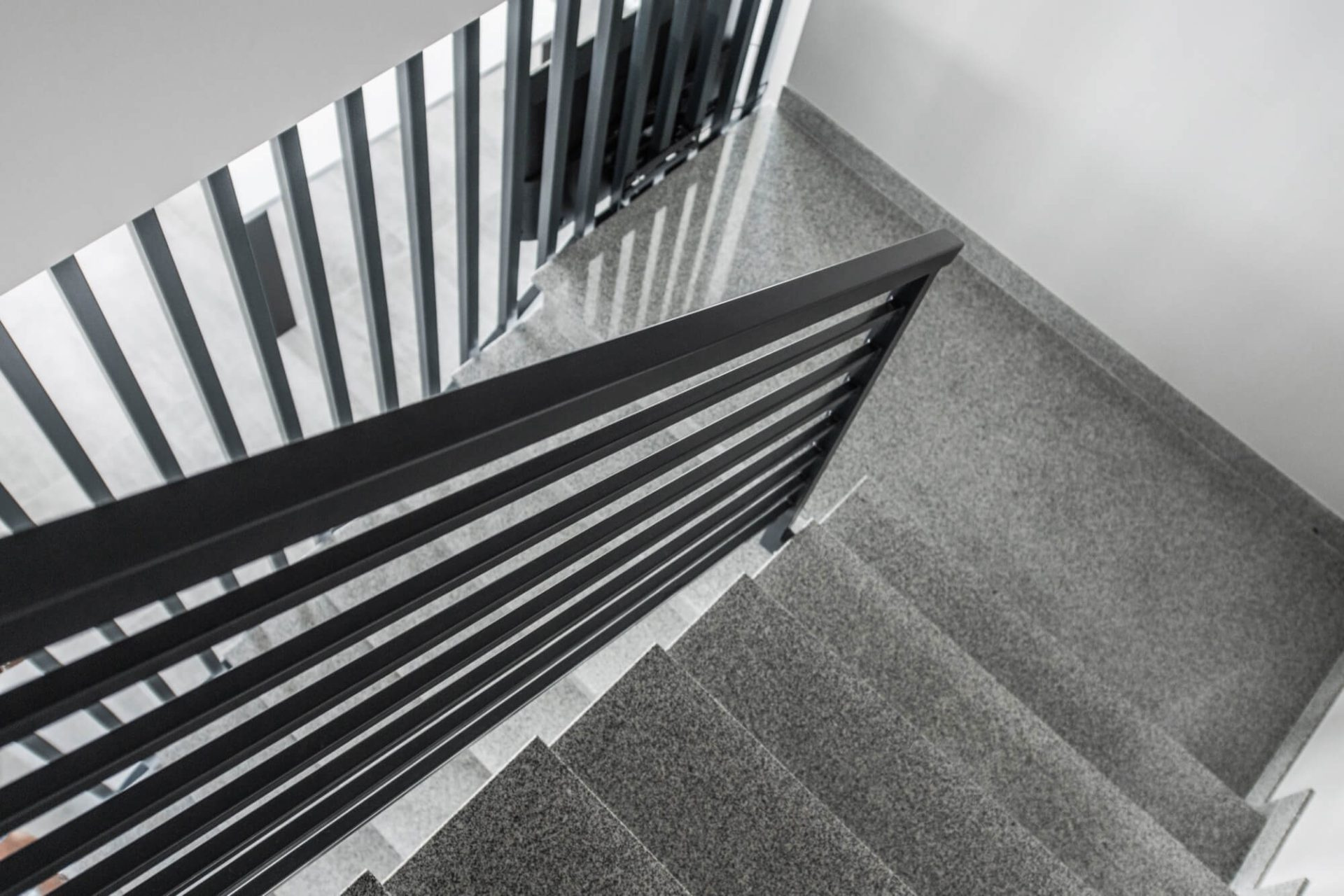 En modern stentrappa med ett svart metallräcke sett uppifrån, ett hållbart val för trapprenovering i offentliga eller privata miljöer.