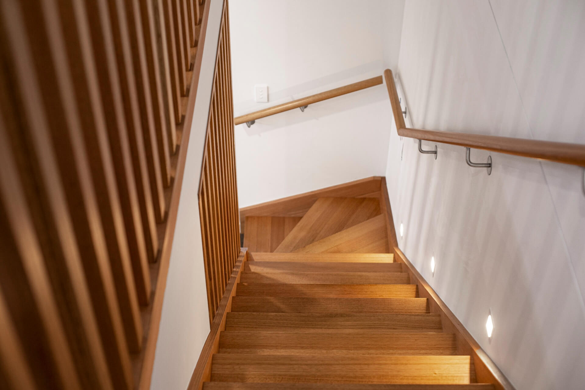 En trätrappa sedd uppifrån med infällda spotlights i väggen, en smart lösning vid trapprenovering.